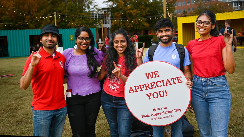 Students pose for group photo with circular white placard with red text reading #packappreciationday.