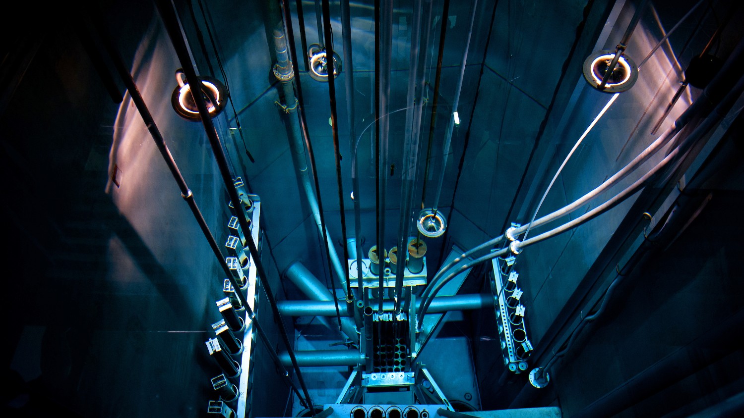 An overhead view looking down into the PULSTAR nuclear reactor lit in bluish light.