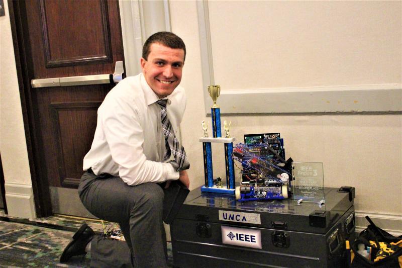 Robert Brenneman at IEEE competition posing with his robot and trophy.