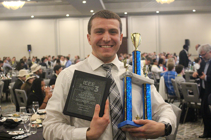 Robert Brenneman at IEEE competition holds the plaque and trophy that he was awarded.