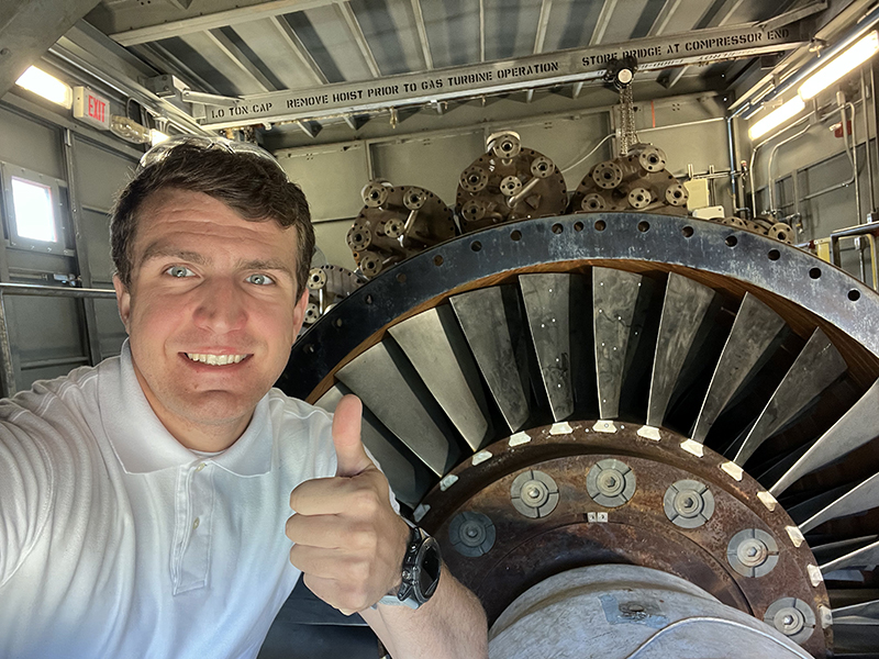 Robert Brenneman gives thumbs up while posing next to a jet engine.