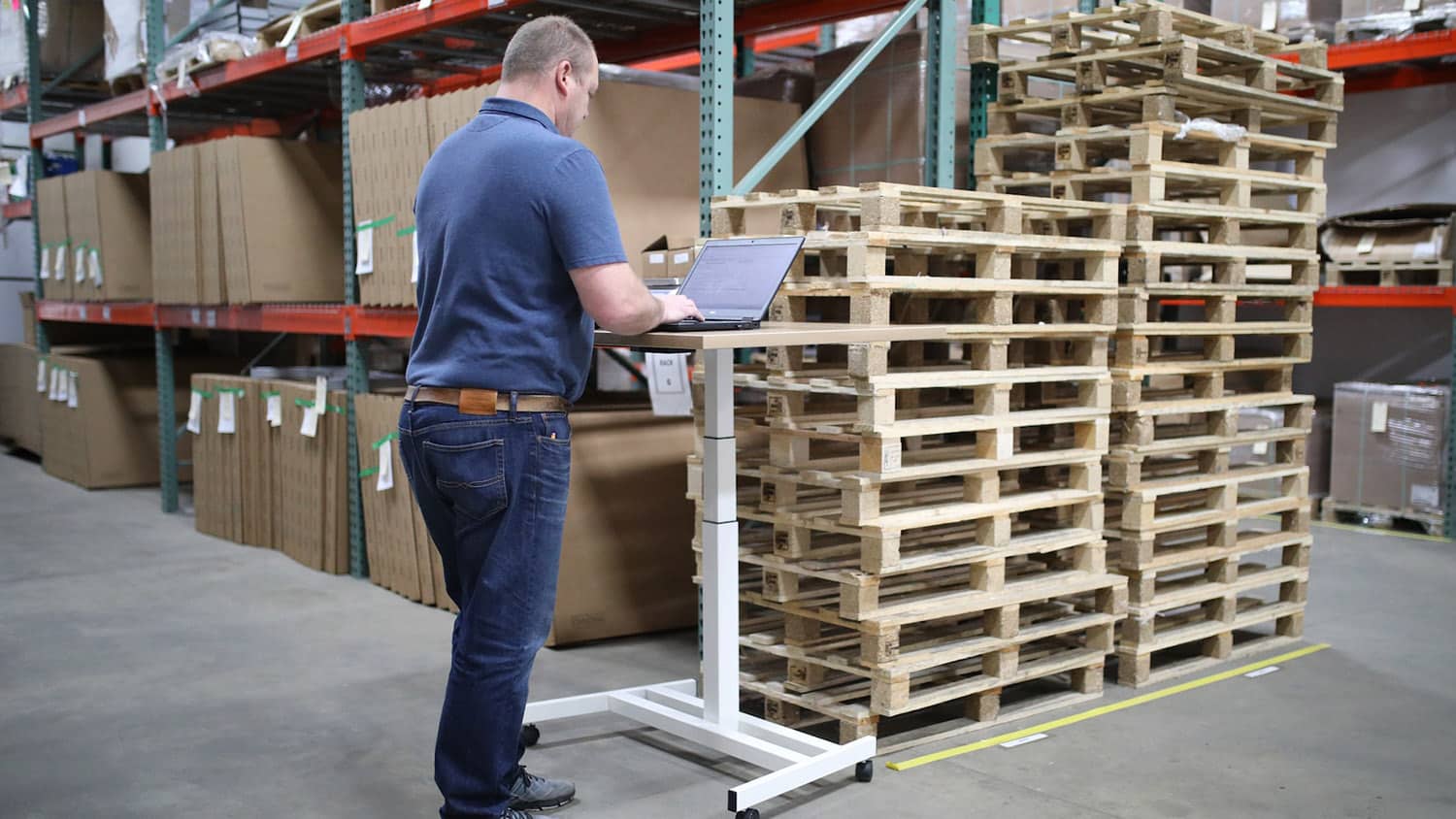 Man in a shipping warehouse looks at a laptop computer.