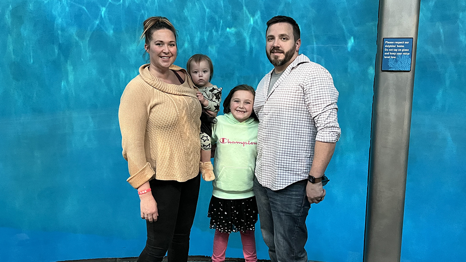 Kye Nielsen, right, poses with his family in front of a large aquarium designed for oceanic life.