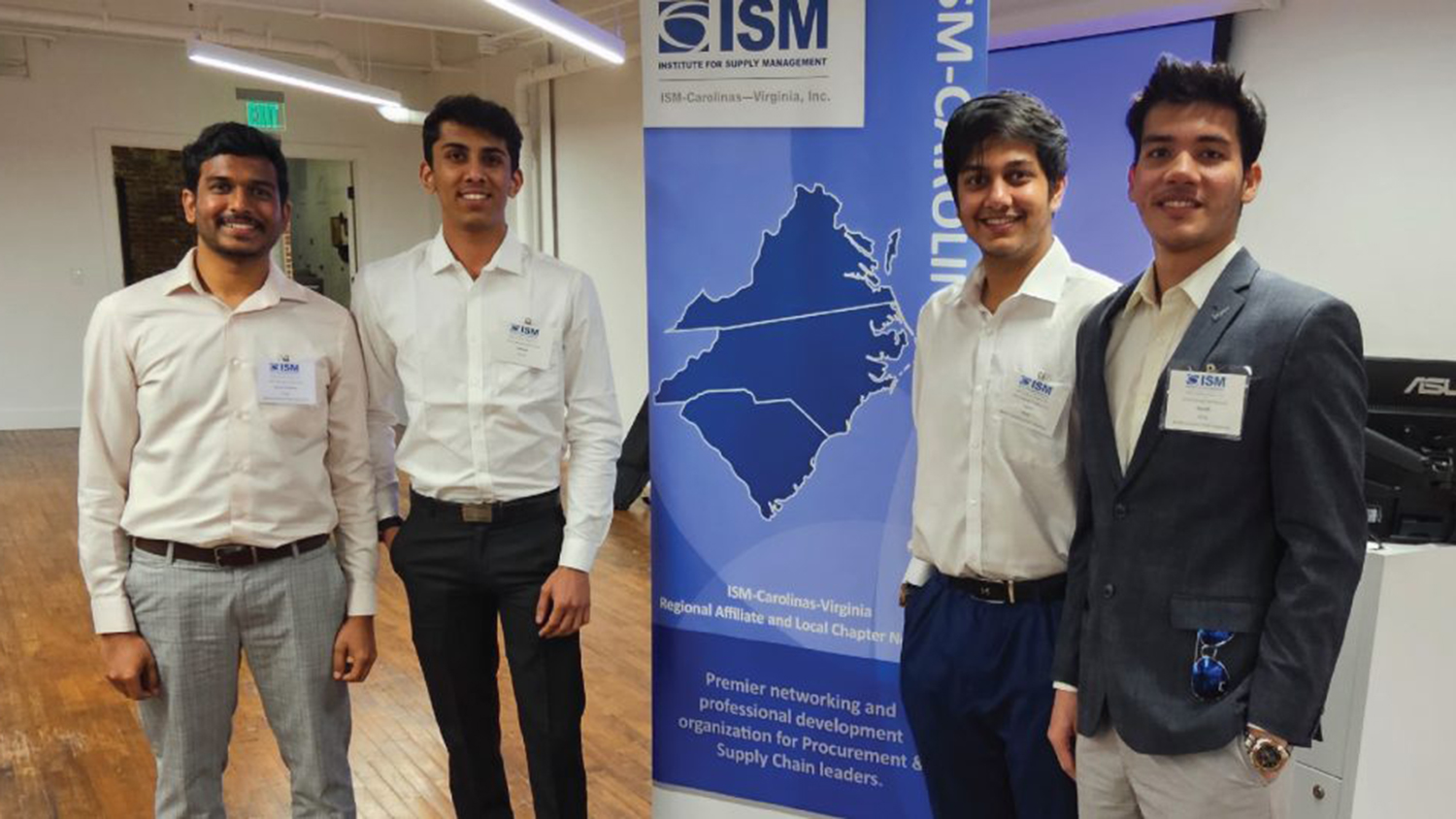 From left: Vamsi Engu, Aakash Dhruv, Parth Aloni and Hardik Birla standing in front of a blue and white ISM banner.