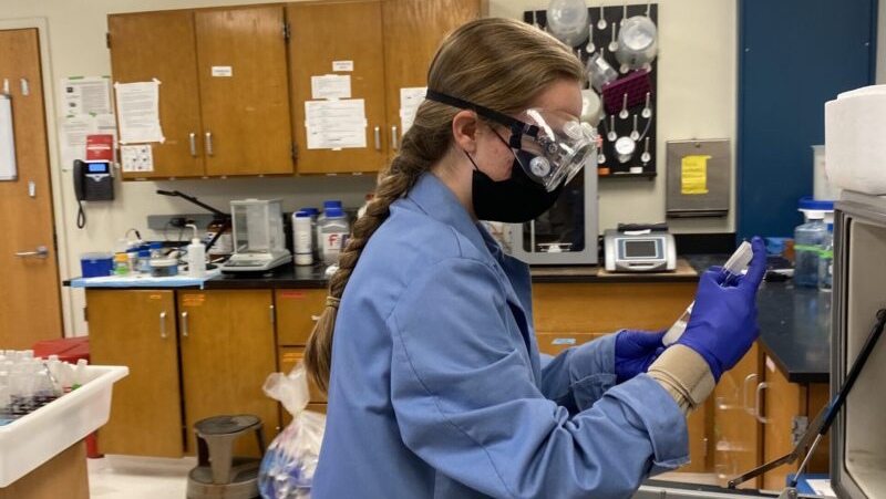 Katie Traynelis dressed in blue protective gear working in a research laboratory.