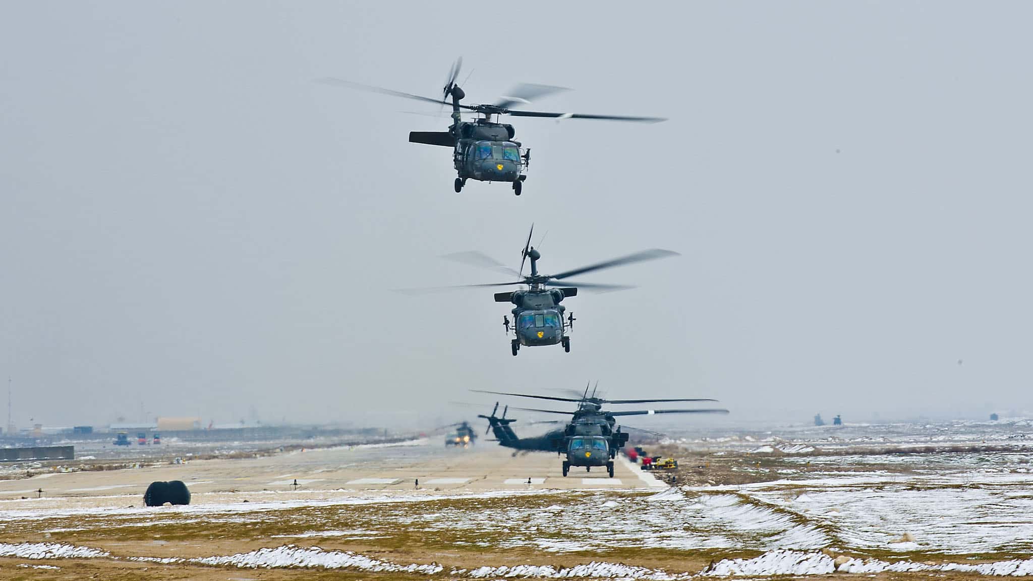 Several military helicopters take off in formation from an airbase.