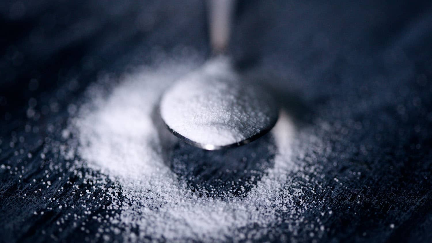 A spoon holds a scoop of white powder over a grey table.