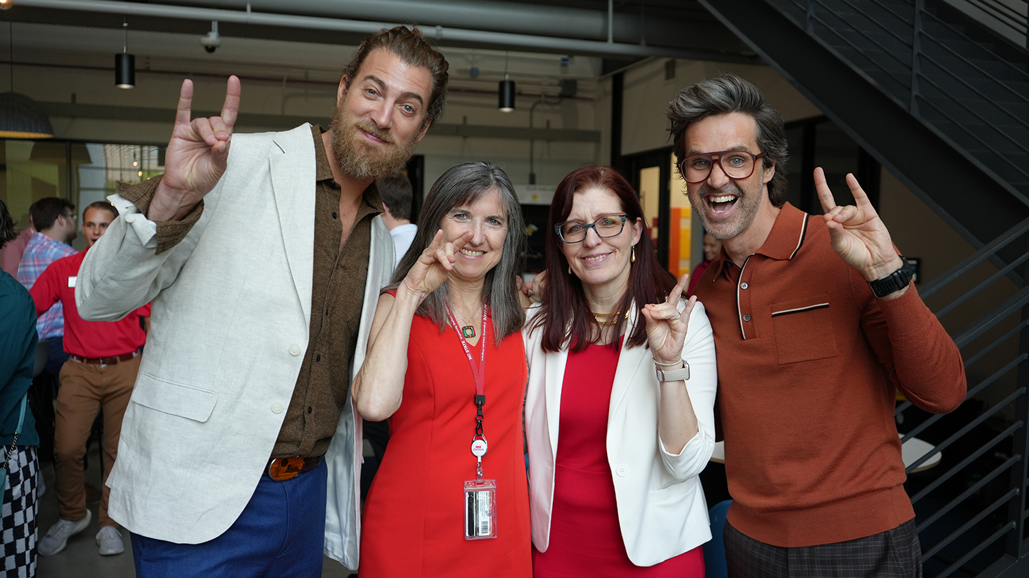 Rhett and Link pose for a photo on either side of department heads Jackie MacDonald Gibson and Julie Swann while all flash the NC State Wolfpack hand sign.