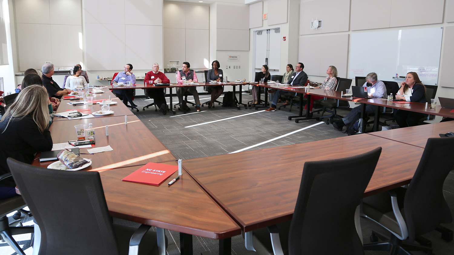 Volunteer leaders meet to discuss strategies and share ideas in a large conference room seated at a series of tables arranged in a square.
