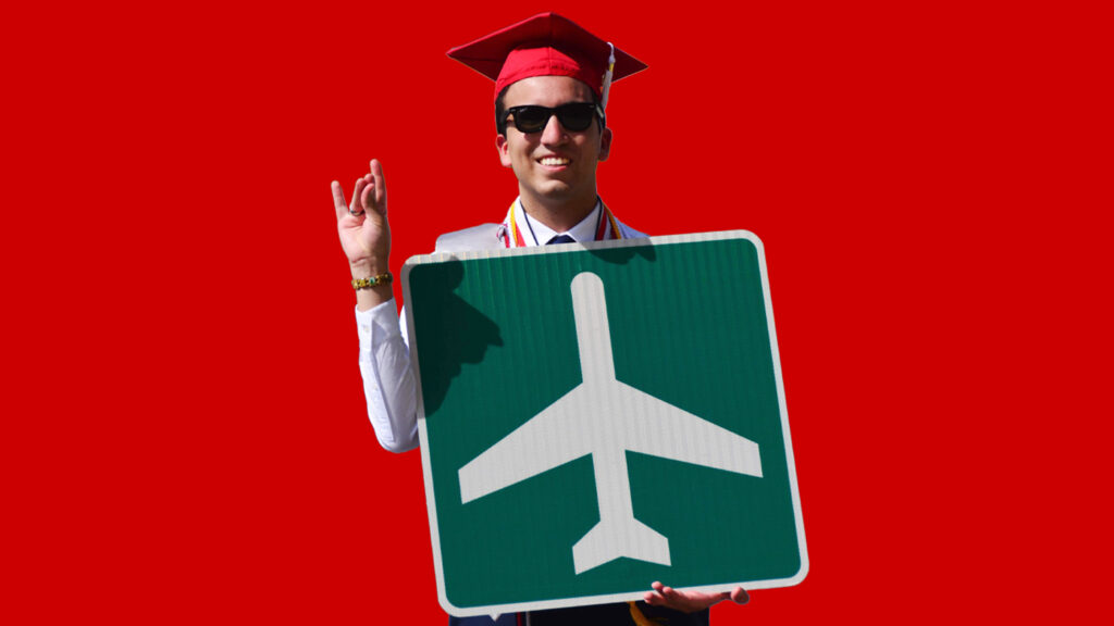 Alberto Quiroga wearing his red graduation cap and holding a green and white airplane directional road sign.