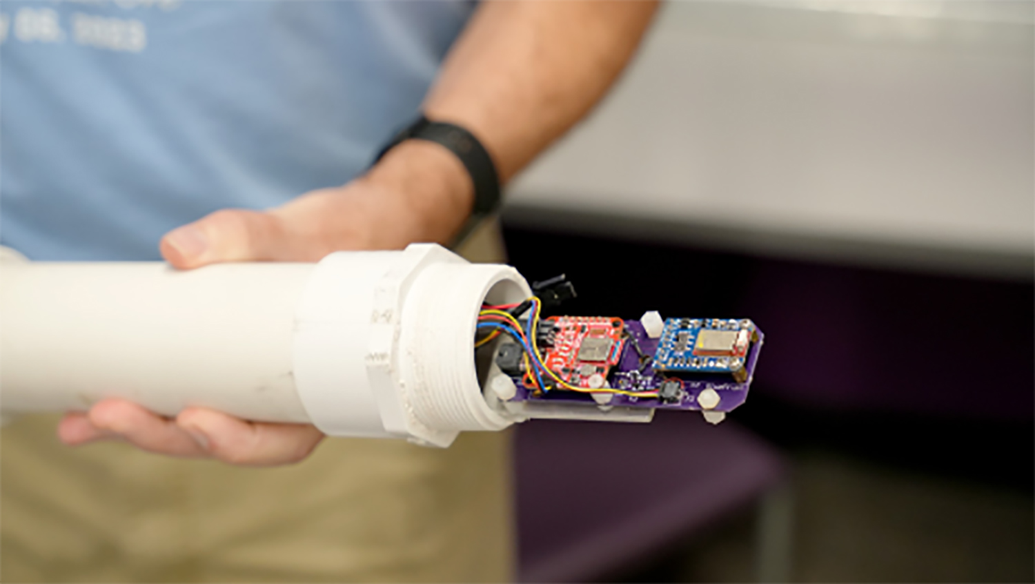 Student holding a large, white PVC pipe with an electronic sensor inside.