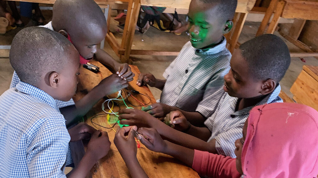 Five Rwandan boys around a table work together on an electrical circuit.