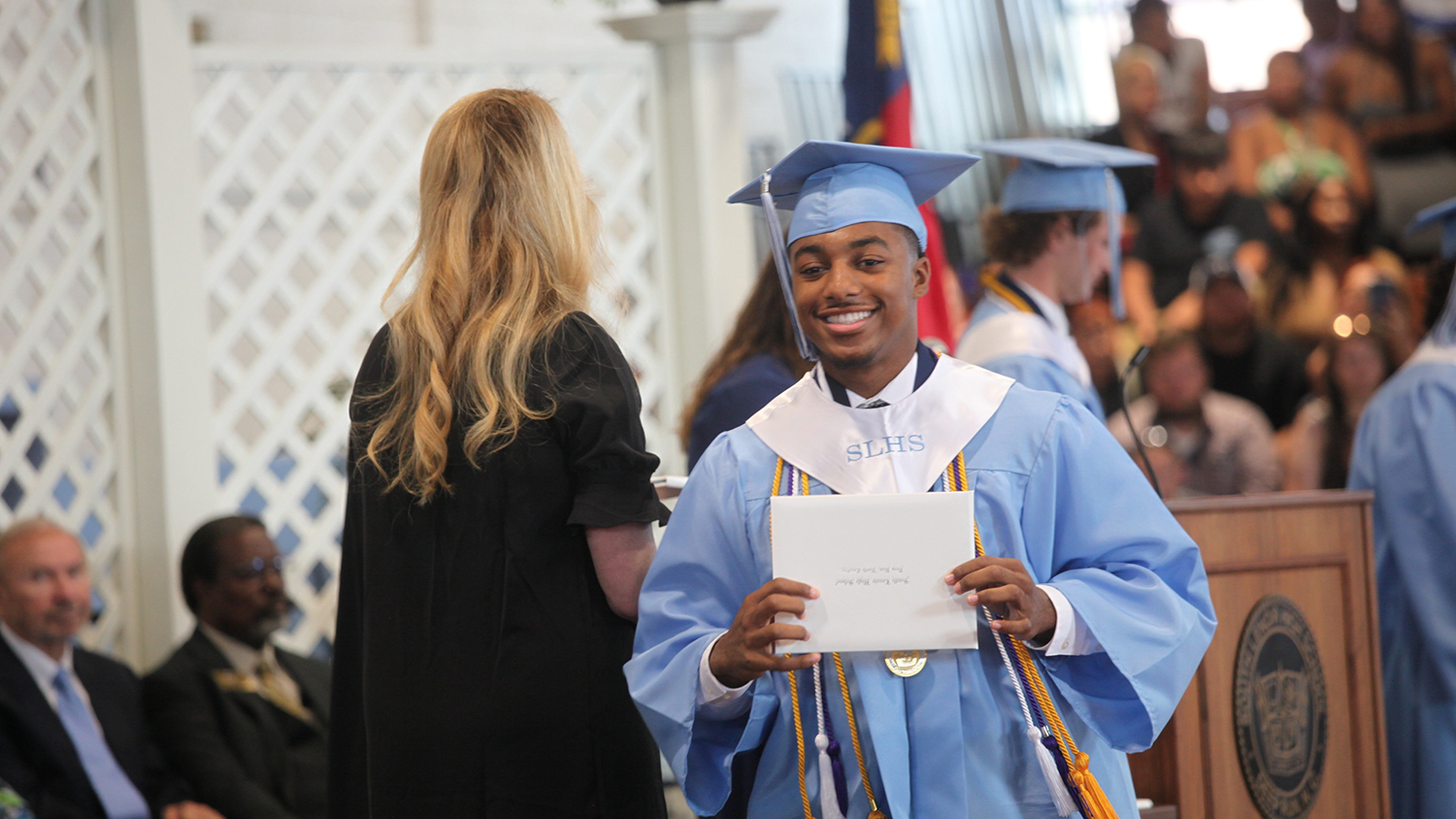 Zaire Garner receiving his high school diploma. He is dressed in a light blue cap and gown.