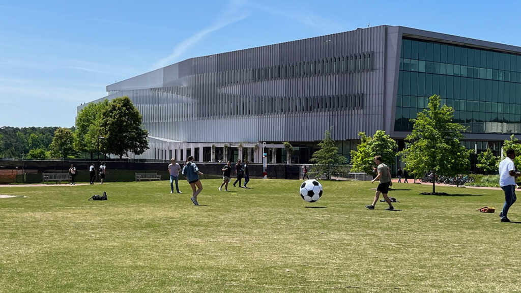 Students play soccer in The Oval with Hunt Library in the background.