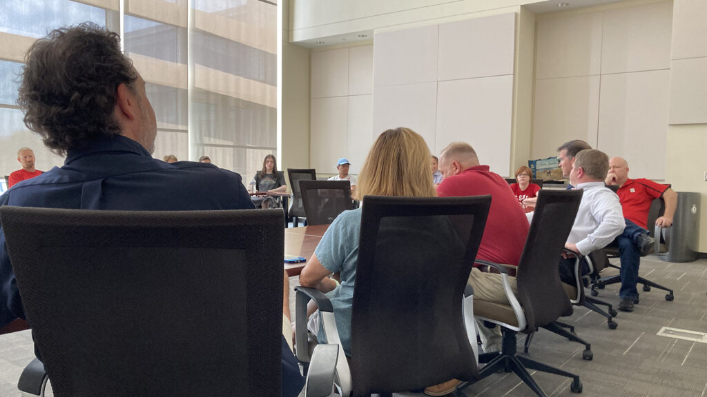 Alumni and former members of the HELIOS project sit at a long conference table.