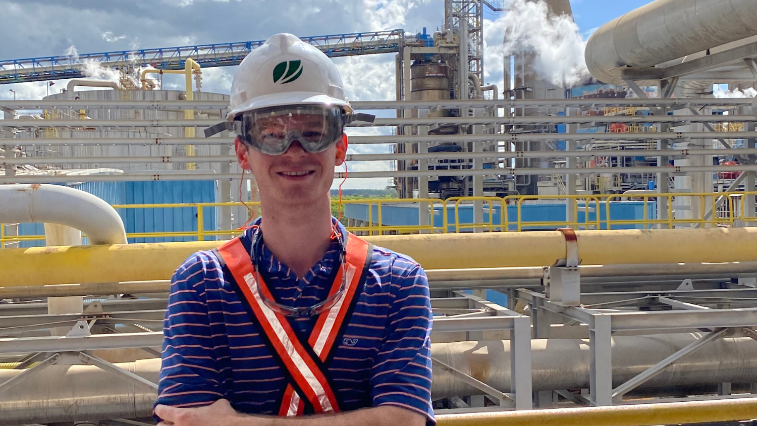 Weston Cregger, wearing a white hard hat, stands in front of an industrial plant.