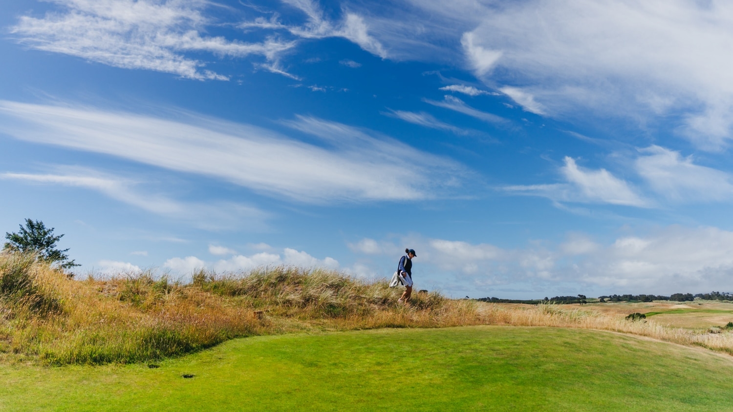 A wide shot shows Caroline Ellington far away walking on some grasslands next to a golf course.