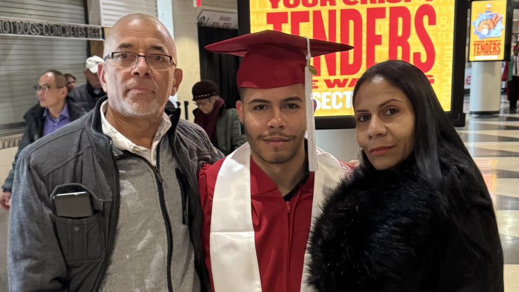 Ramon Sanchez, center, dressed in red NC State graduation gown and cap, poses with his parents.