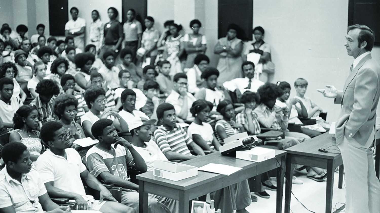 Black and white photo of MEP students attending a class. Professor stands at front while speaking.