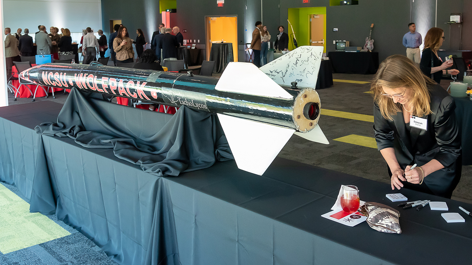 During the College of Engineering 100 year celebation, a woman completes a small registration form next to a large scale model rocket used by the NC State rocketry club.