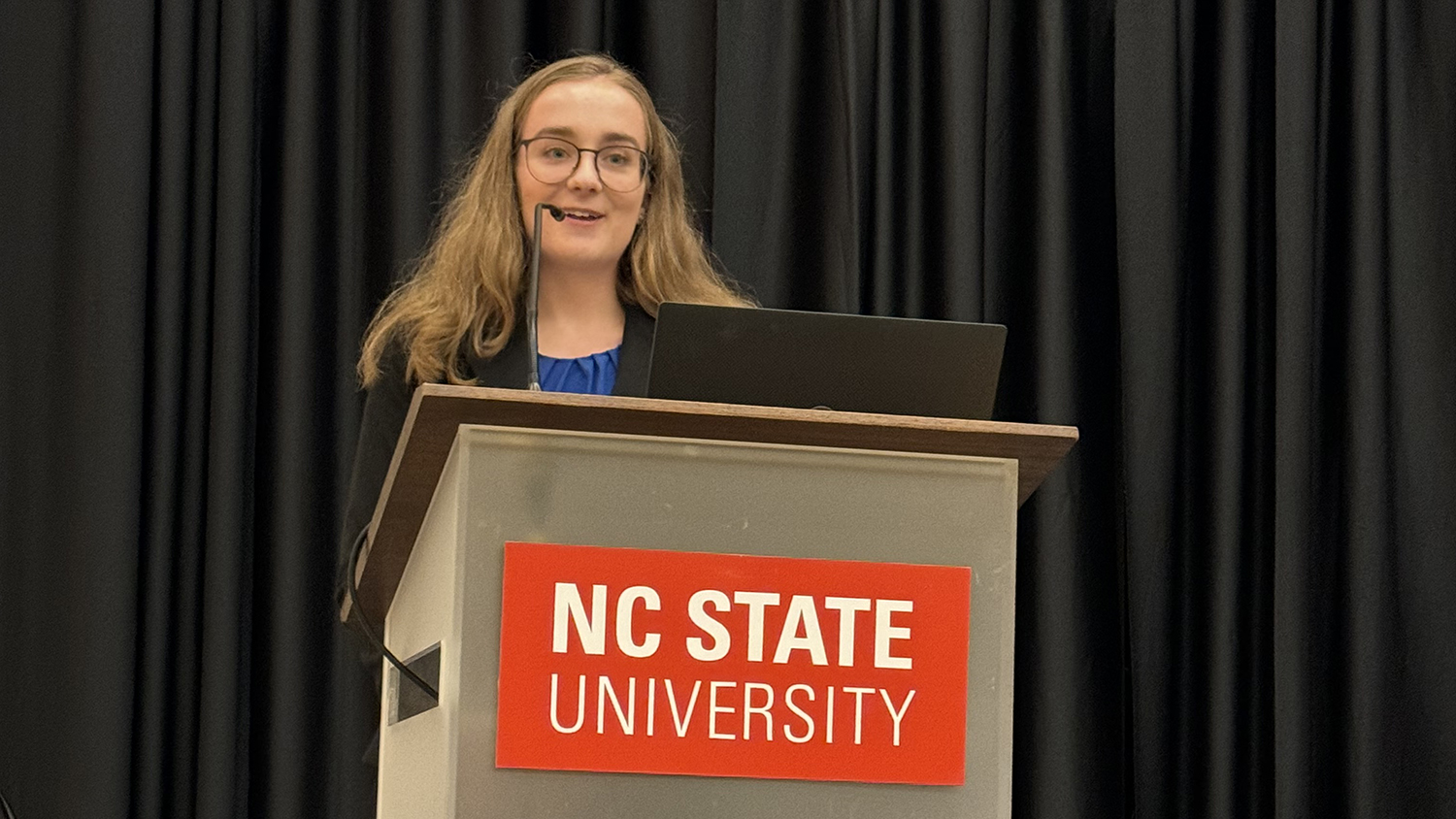 Katherine Traynelis speaks from behind a NC State University branded lecturn.