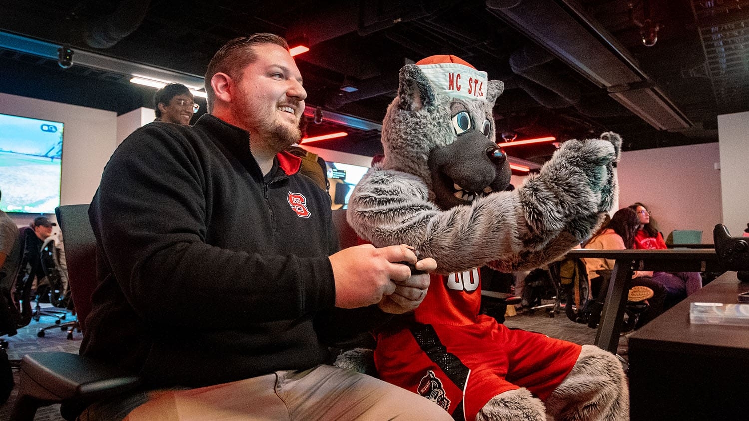 NC State Esports Program Director Cody Elsen plays a game alongside Mr. Wuf in the NC State Gaming and Esports Lab.