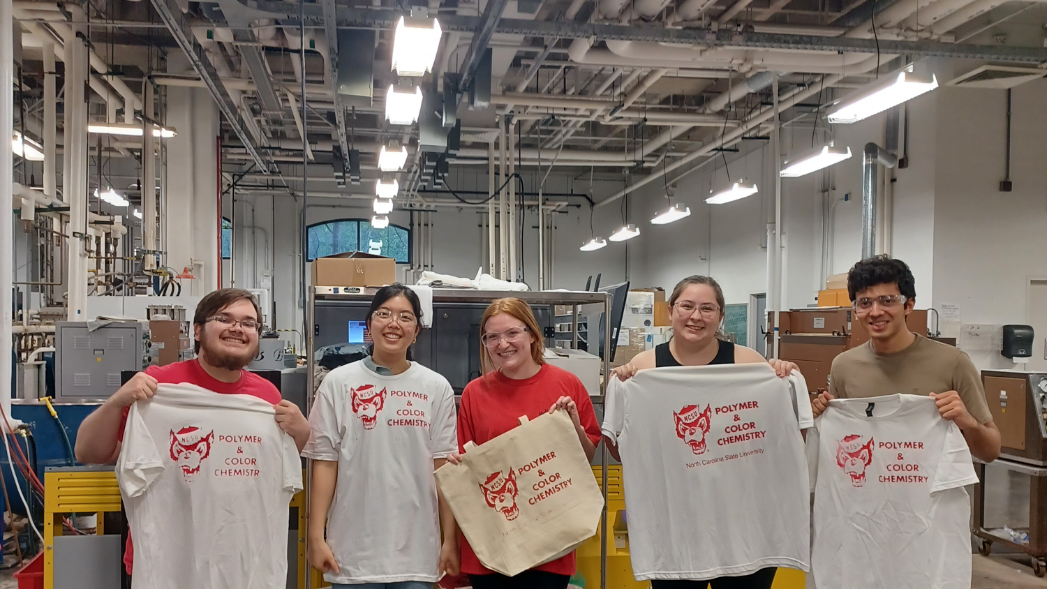 PCC students in the dyeing and finishing lab hold screen printed tote bags and t-shirts.