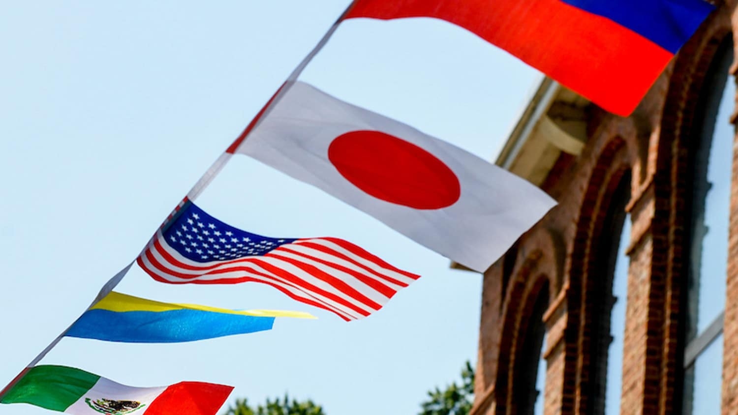 The American and Japanese flags blow in the wind on a line next to a brick building on campus