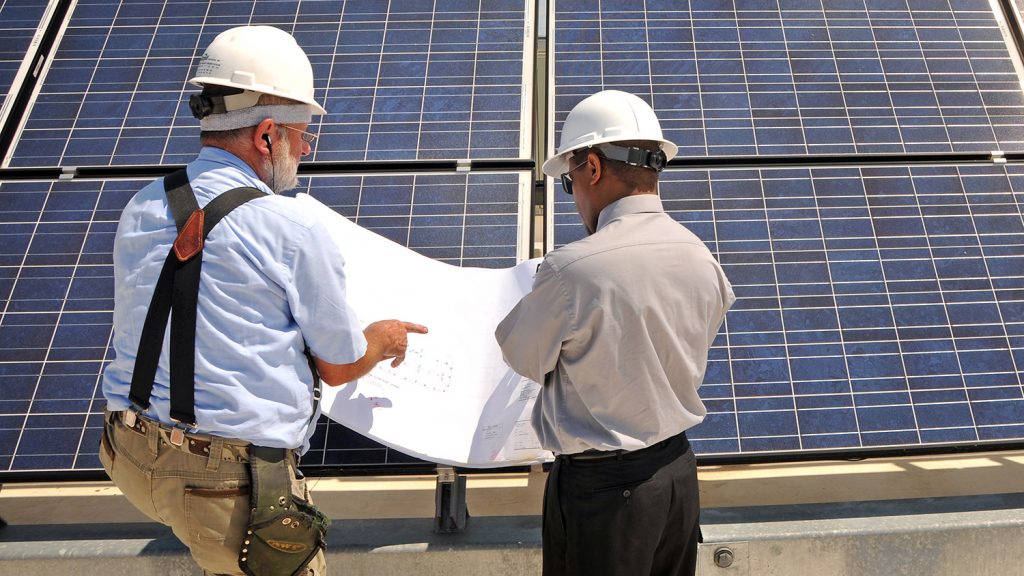 Two engineers reviewing large printout of schematic while standing in front of several large solar panels.