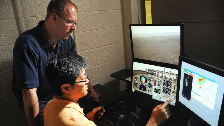 Dr. Dave Kaber looks over a graduate student's shoulder as they test a flight simulator in the ISE department.